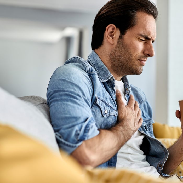 young man feeling sick holding his chest pain while drinking tea living room